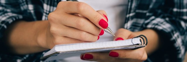 Woman in plaid shirt and a red manicure pen writing in a notebook