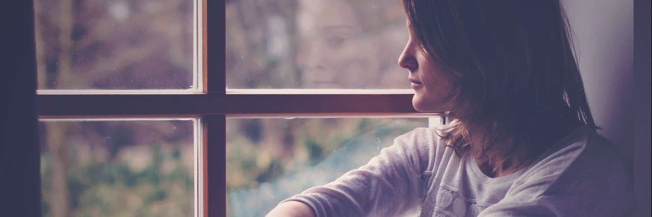 young woman looking out window lonely sad