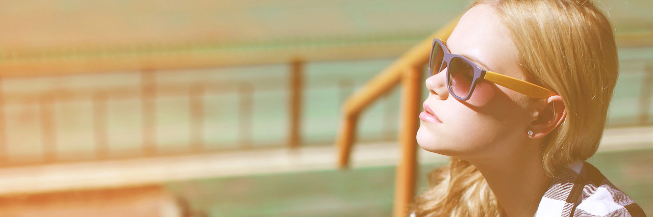 Navigating the Five Stages of Grief With Vision Loss Thoughtful woman in sunglasses sitting outside on stairs.