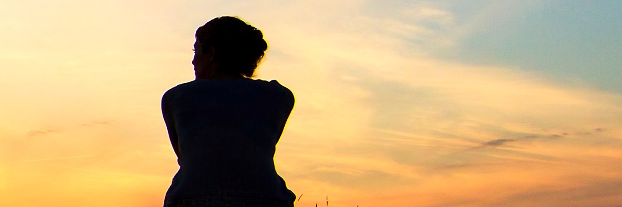 What Grief Can Be Like for a Bereaved Parent Silhouette of woman sitting on grass in front of sunset sky