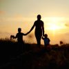 Mom holding hands with two children near a grassy area at sunset