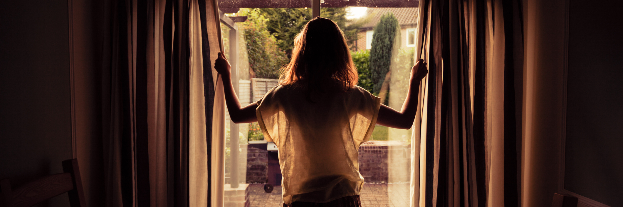 woman opening curtains at sunrise