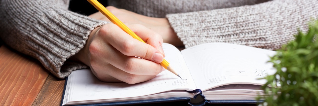 female hands with pencil writing on notebook.