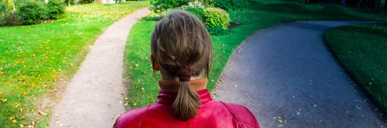 5 Tough Choices You Face When You're Chronically Ill or in Pain Girl in red jacket standing on the fork of two roads.