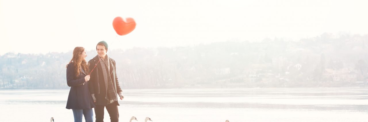 Cute young couple in love, walking at the riverside, with a red balloon and swans