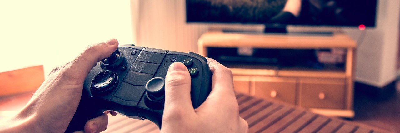 Hands holding game pad and playing shooter game on tv screen.