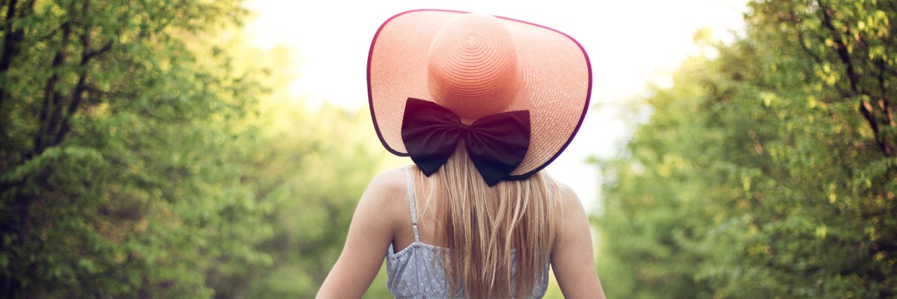 Why I'm 'Happy to Be Here' – Regardless of My Health Woman in sundress, facing away from camera, wearing a hat with a big blue bow on the back.