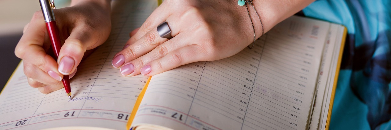 woman in blue dress writing her schedule in a day planner