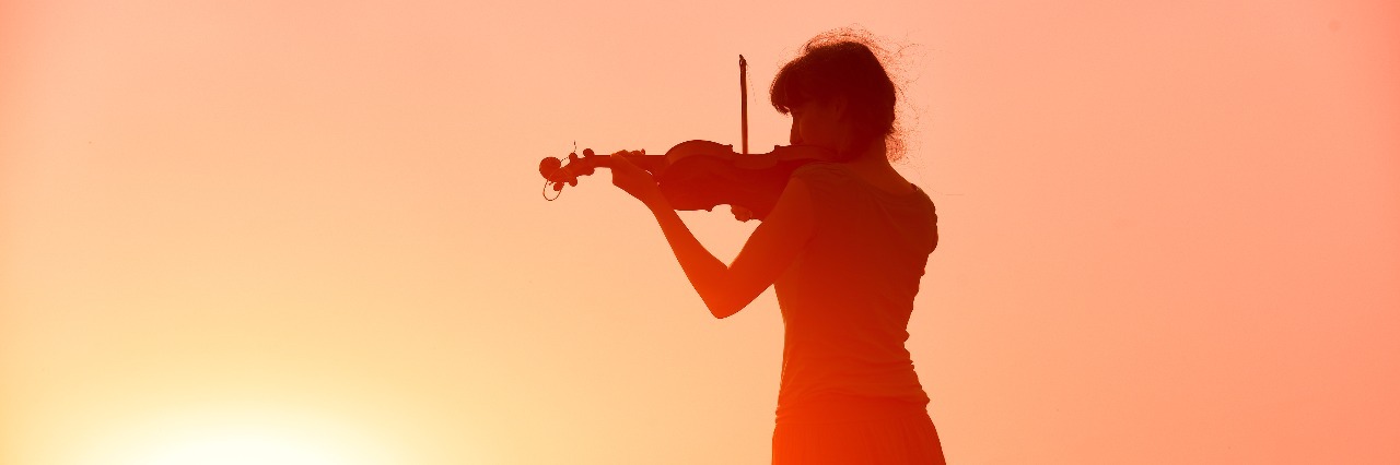 woman playing a violin in a field in front of a sunset