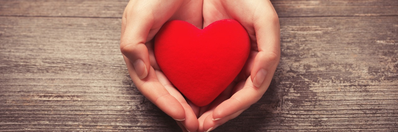 Importance of Kindness for People With Rare Disease hands holding small red heart against wooden table