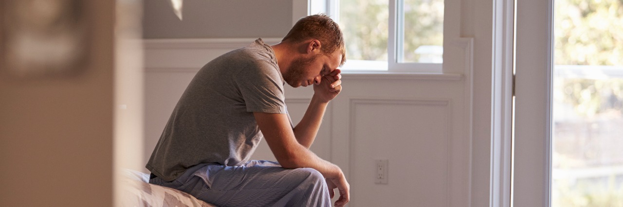 man sitting on bed with head in hands