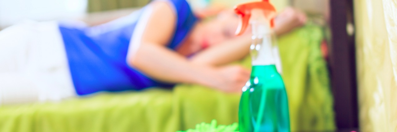 woman lying on bed with cleaning supplies on table