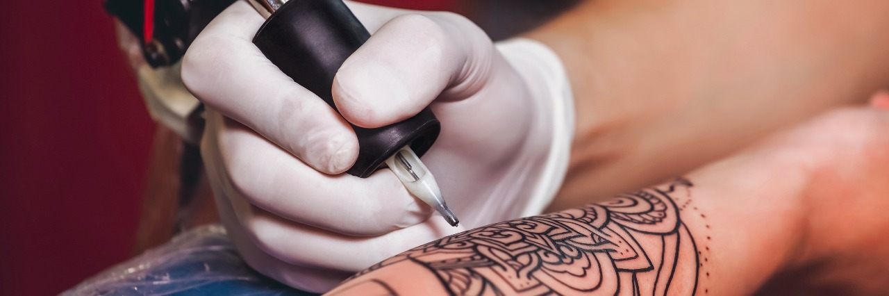 Why Getting Tattoos Helps My Self-Harm Recovery Tattoo master protective gloves make a tattoo in black ink on the hand of the girl. Close-up.