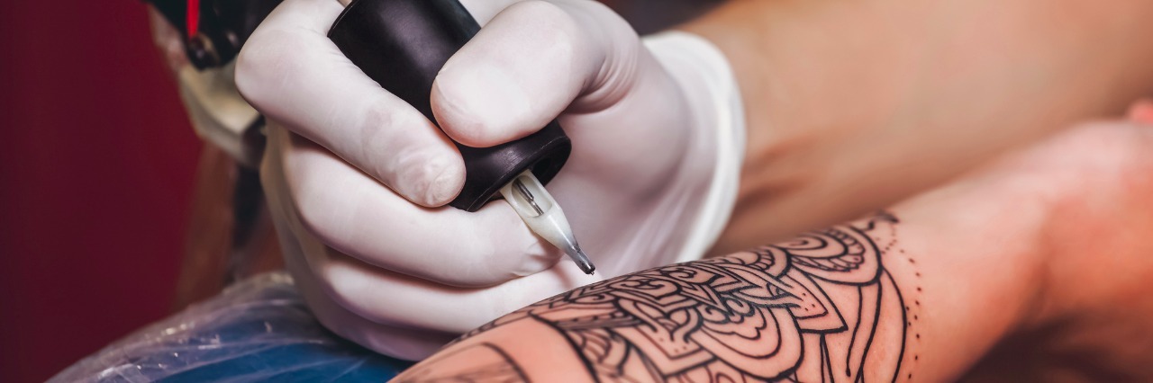 Why Getting Tattoos Helps My Self-Harm Recovery Tattoo master protective gloves make a tattoo in black ink on the hand of the girl. Close-up.