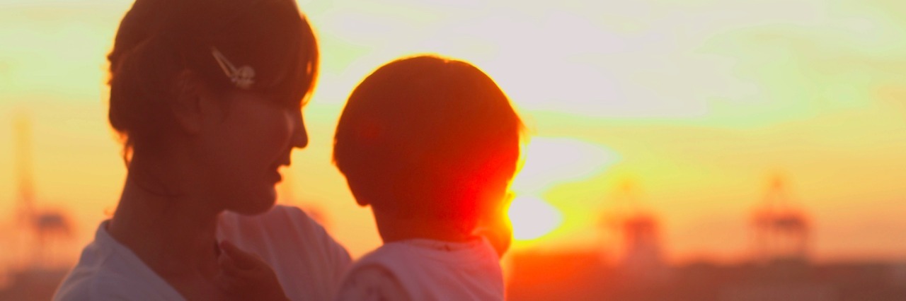 My Son Is on the Autism Spectrum, and He's Wonderful in Every Way Mother holding child, with water and sunset landscape in the background