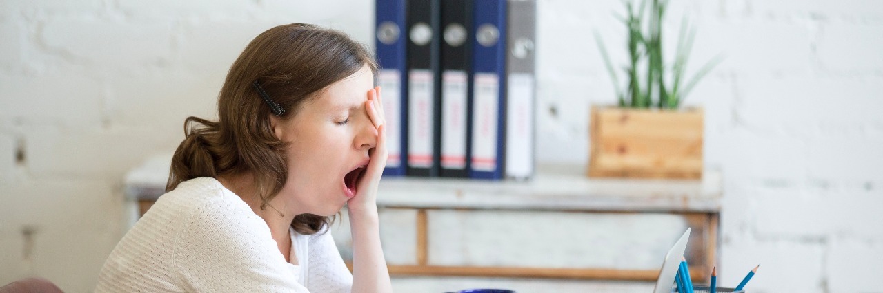 When I Realized I Overworked Myself to Distract From Depression Portrait of young woman sitting at table in front of laptop, sleepy