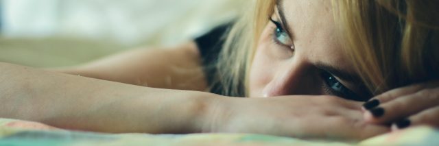 woman with blonde hair lying in bed looking upset