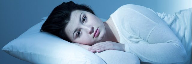 tired young woman lying in bed with eyes open