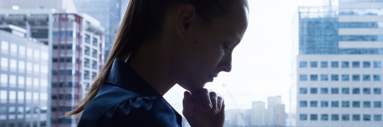 silhouette of upset woman standing next to a window overlooking the city