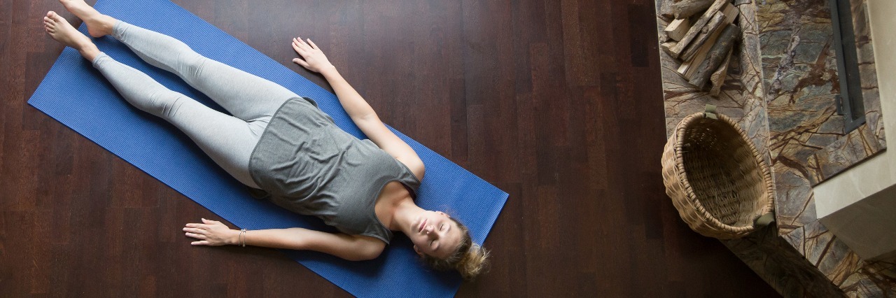 young woman performing yoga savasana pose relaxation on wooden floor near window