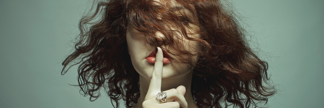Woman on gray background with finger pressed to her lips