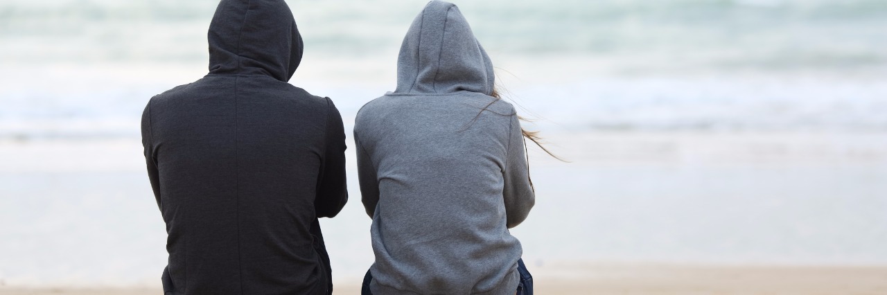 Afraid to Tell Friend About Mental Illness Diagnosis two teenagers on beach sitting back to back staring at ocean bad weather