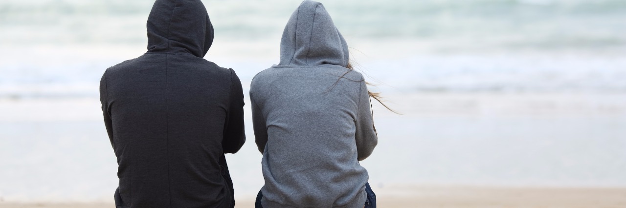 two teenagers on beach sitting back to back staring at ocean bad weather