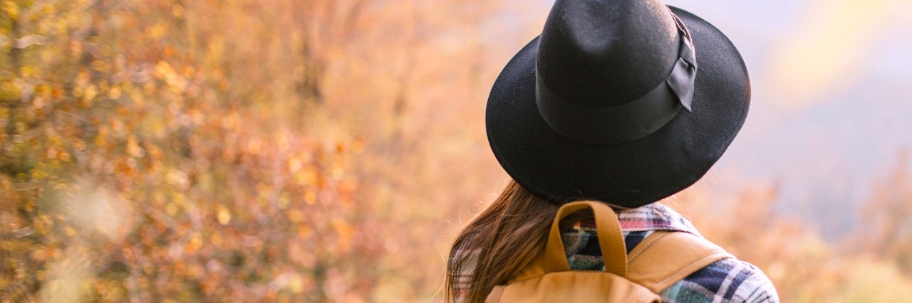 My Experience as a Young Adult on the Autism Spectrum Woman wearing hat and backpack, walking near autumn trees in park