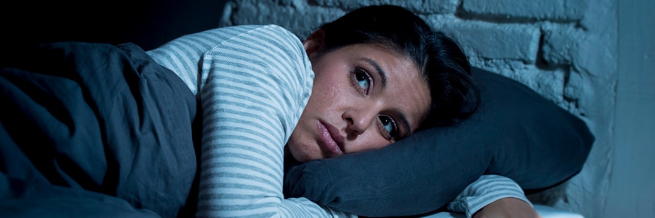 Going to Sleep With PTSD Can Trigger My Flashbacks young beautiful hispanic woman at home bedroom lying in bed late at night trying to sleep suffering insomnia sleeping disorder or scared on nightmares looking sad worried and stressed