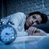 woman lying in bed with eyes open next to a clock