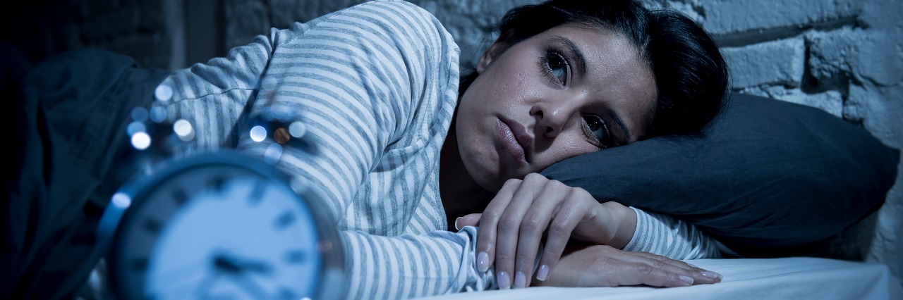 Struggling With Insomnia and Remaining Optimistic woman lying in bed with eyes open next to a clock