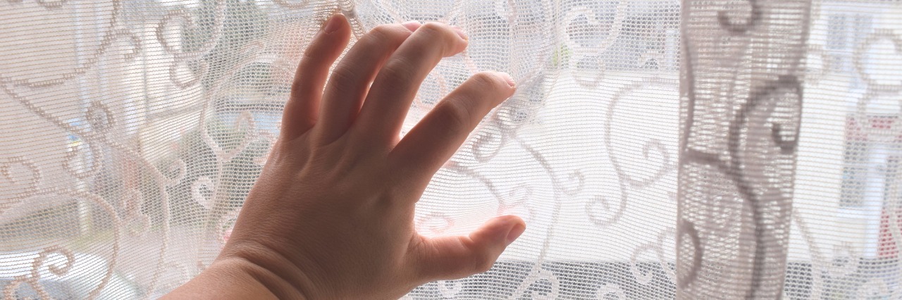 Isolation of Living With Ankylosing Spondylitis, Ehlers-Danlos woman's hand over a curtain on a window looking out over the street