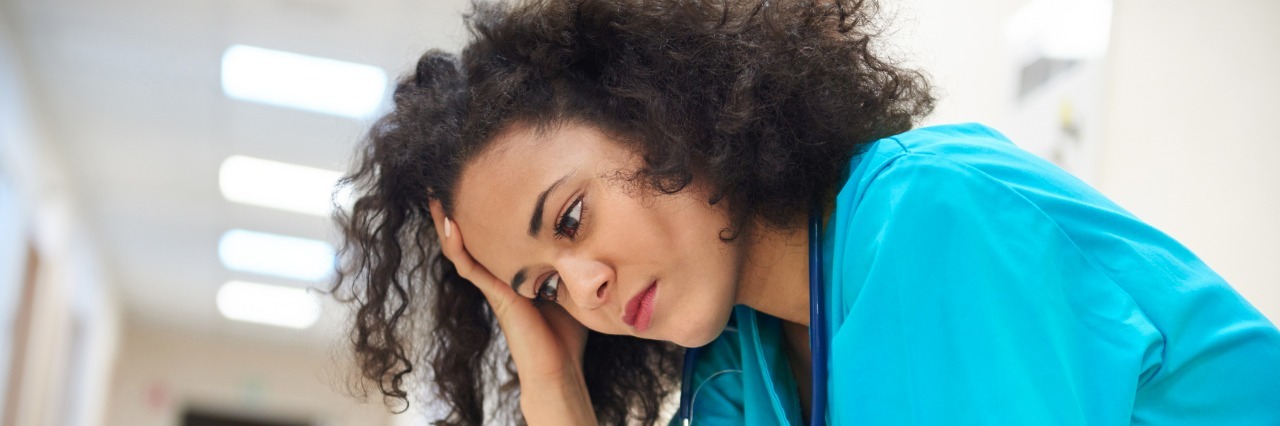 Dear Healthcare Employer: What I Wish I Could Tell You About My Health A nurse sits in hospital hallway, looking upset and defeated