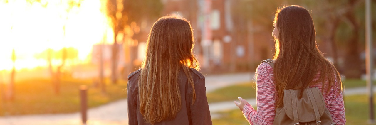 A Letter to My Best Friend Who Sees Past My Chronic Illness back view of two friends walking together in a park at sunrise with a warm light in the background