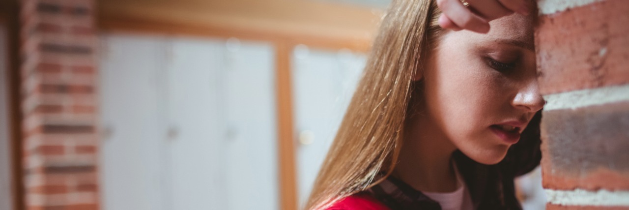 An Average Day in High School With Fibromyalgia Student leaning on brick wall at school, looking tired.