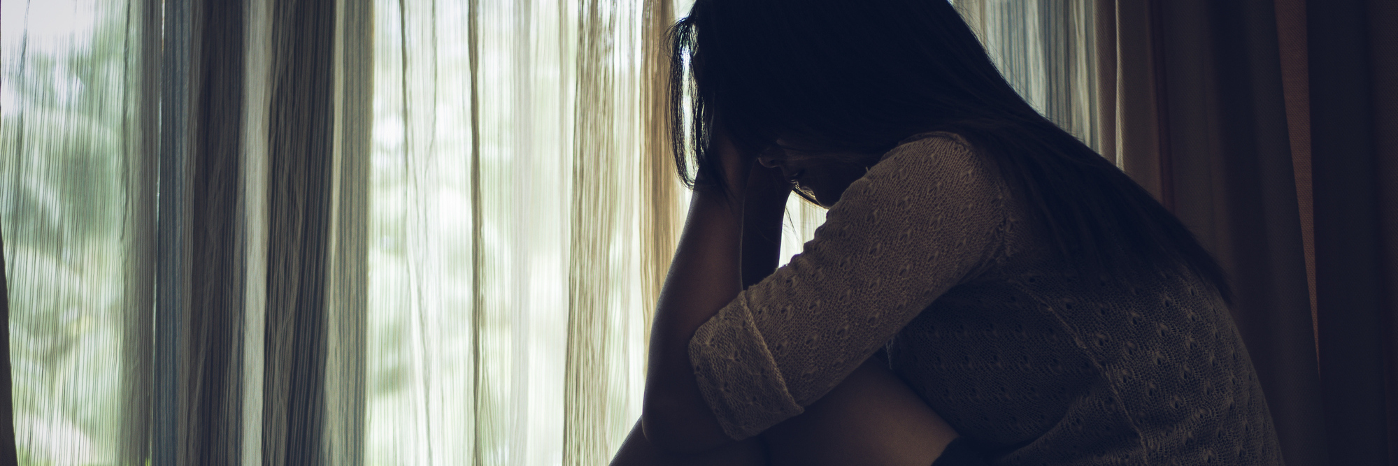 My Problem With 'Post-Traumatic Growth' as an Individual With PTSD woman sitting on floor hugging knees next to window