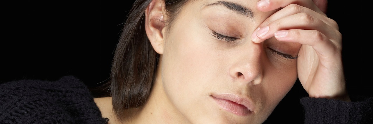 Woman with a headache, eyes closed, hand across forehead