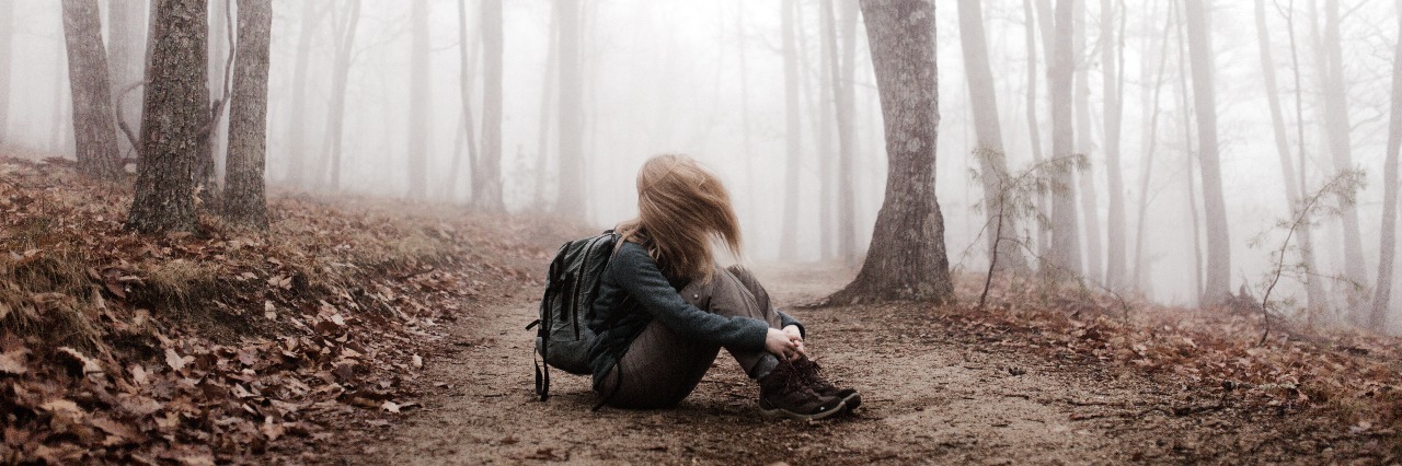 girl sitting alone in forest fog with hair covering face