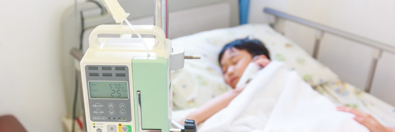 I'm Not Strong, My Son Is Little boy sleeping in hospital bed, his image is blurry, in focus and forefront is an infusion pump