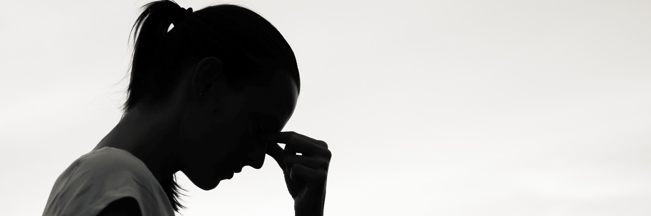 Having Hard Days After Surviving Cancer silhouette of the profile of a woman with head bent down and her hand to her temple as in frustration