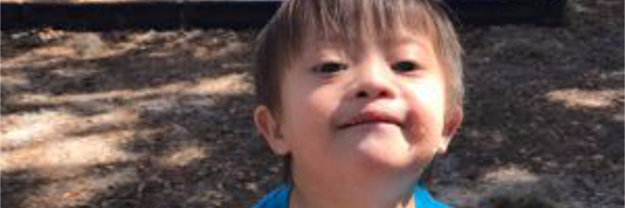 My Son With Down Syndrome Does Not Fit Your Stereotype Little boy with Down syndrome wearing a blue shirt and holding a sandwich