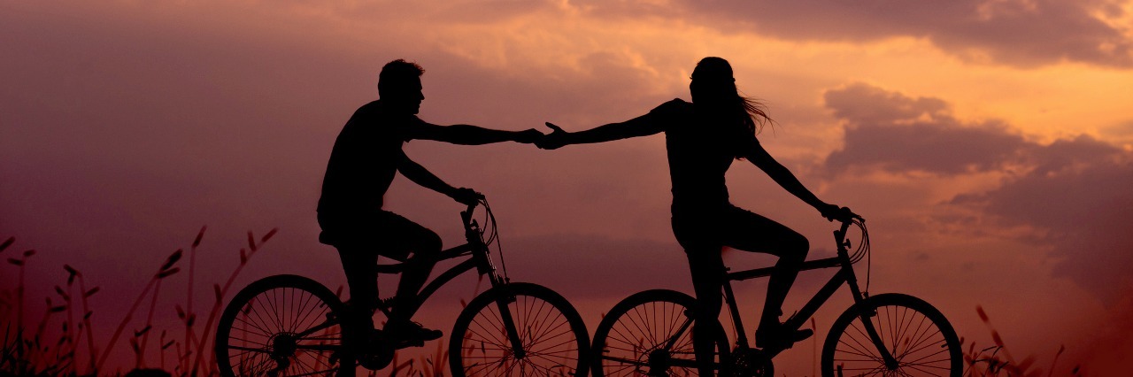 man and woman riding bikes at sunset reaching out to each other romance
