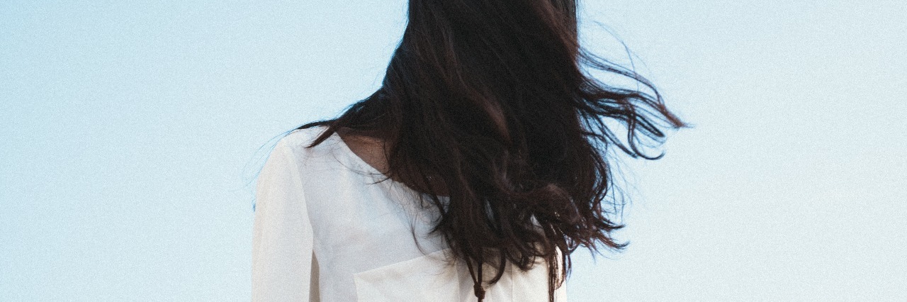 young woman with hair covering face against sky backdrop