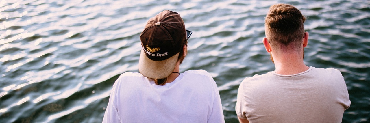 Two men friends sitting looking at ocean together support concept