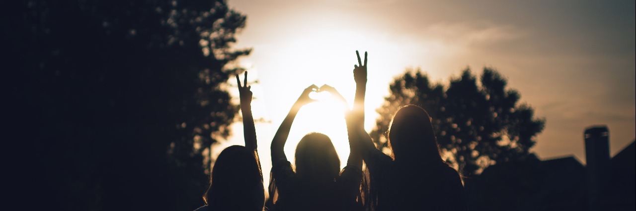 friends silhouetted against sunset with peace and heart signs