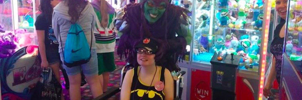 girl in batman shirt in wheelchair with person wearing mask standing behind her at arcade