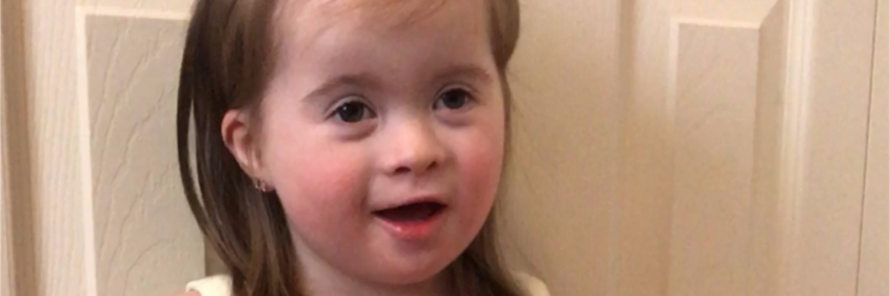 If I'd Known Then What I Know Now About My Daughter With Down Syndrome Little girl with Down syndrome standing in front of a white door wearing an Easter dress