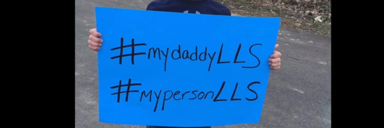 Little boy holding a blue sign that reads, "#mydaddyLLS" and "mypersonLLS"