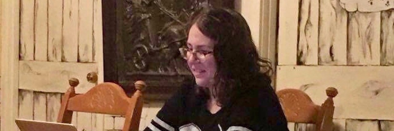 Rising From the Ashes: My Journey With Autism and HSAM Rebecca sitting in her dining room table with a laptop open in front of her.