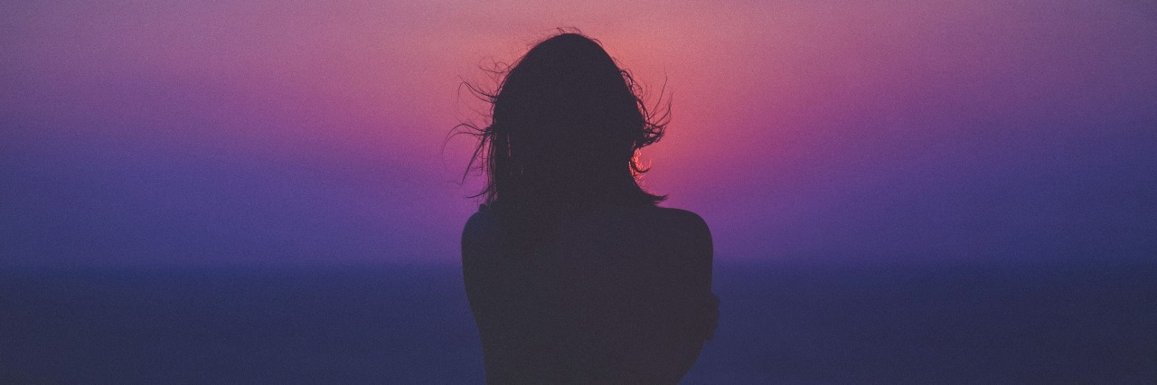 woman facing purple and pink sunset silhouetted against sky